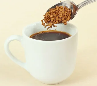 Instantkaffee, der mit einem Löffel in eine Tasse gegeben wird