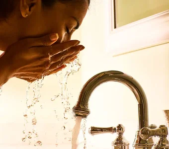 Junge Frau wäscht sich ihr Gesicht mit Wasser
