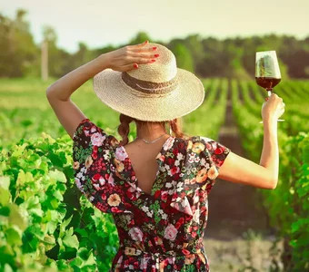 Eine Frau geht mit einem Weinglas in der Hand durch ein sommerliches Weingut