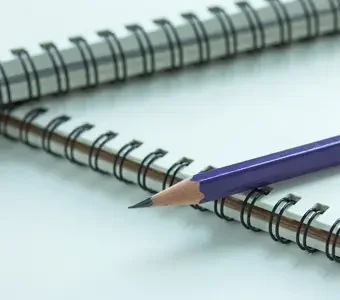 Zwei per Drahtkammbindung gebundene Hefte nebeneinander mit aufliegendem Bleistift