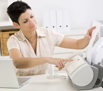 Eine Frau sitzt am Schreibtisch und legt ein Dokument in ein Faxgerät ein
