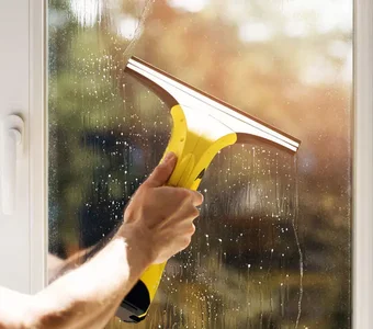 Ein junger Mann putzt seine Fenster mit einem modernen Fenstersauger