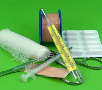 Arrangement aus Fieberthermometer, Verbandsmaterial, Tabletten und Pinzette vor grünem Hintergrund