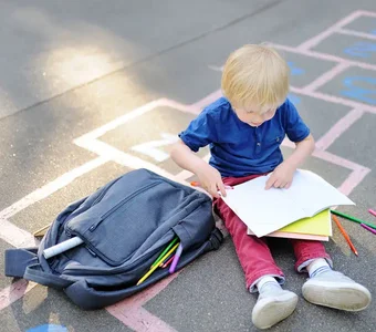 Ein kleiner Junge sitzt auf dem Boden neben seinem Rucksack und malt