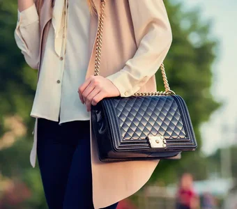 Eine elegante bekleidete Frau im Park trägt eine Leder-Handtasche