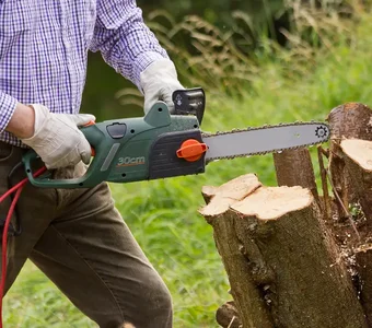 Eine elektrische Kettensäge wird dazu benutzt, einen Baumstumpf weiter zu zerkleinern