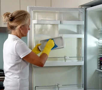 Blonde Frau reinigt ihren Kühlschrank gründlich mit einem Schwamm