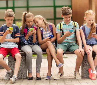 Fünf Schulkinder sitzen auf einer Bank und jedes Kind hält ein Handy in der Hand und guckt darauf