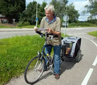 Herr auf Fahrradweg - mit Fahrrad und Hund im Anhänger - sucht eine Route mit Hilfe einer Karte