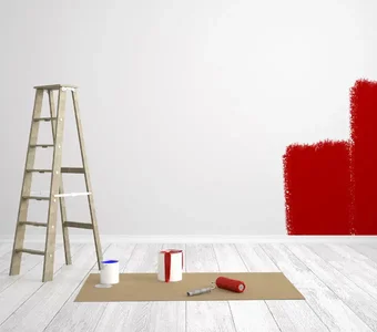Farbeimer, Farbrolle und Leiter in einem Raum, dessen weiße Wand teilweise mit roter Farbe überstrichen ist