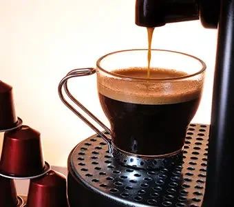 Nahaufnahme einer Kapselmaschine, aus welcher gerade Kaffee läuft.