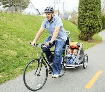 Vater fährt Fahrrad mit zwei Kinder, die sicher im Anhänger sitzen