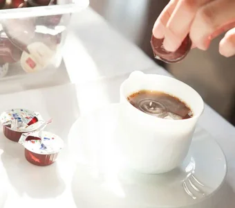 Eine Kaffeetasse und mehrere Kapseln Kondensmilch liegen auf einem Tisch