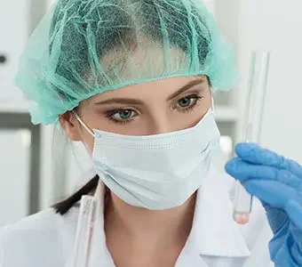 Frau in Laborkleidung schaut auf Flüssigkeit in einem Reagenzglas