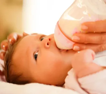 Weibliche Händen halten ein Fläschchen, Baby trinkt