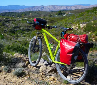 Grünes Fahrrad mit roten Packtaschen steht vor einer hügeligen Landschaft