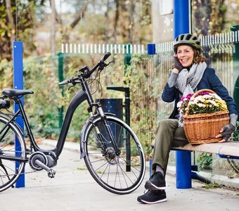 Frau sitzt telefonierend auf einer Bank neben ihrem E-Citybike