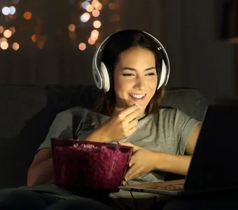 Frau trägt Kopfhörer und schaut einen Film auf ihrem Laptop