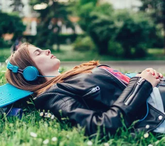 Teenagerin liegt im Park auf ihrem Skateboard und hört Musik