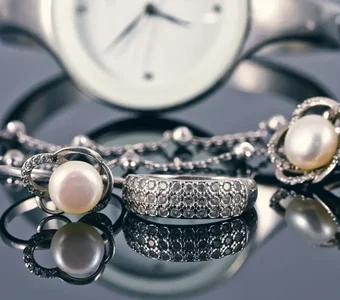 Auf einer spiegelnden Oberfläche liegen verschiedene Schmuckstücke und eine Armbanduhr in Silber