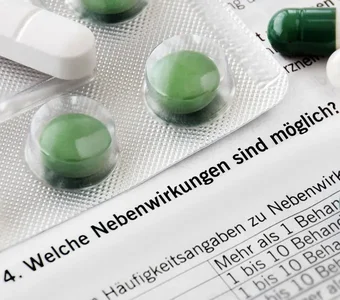 Unterschiedliche Tabletten liegen auf dem Beipackzettel, auf dem das Wort Nebenwirkungen zu lesen ist