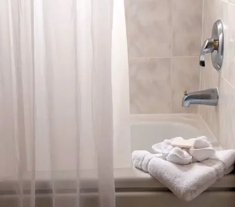 Kunststoff-Duschvorhang vor eine Badewanne, bei der Handtücher und Seife fürs Baden bereit liegen