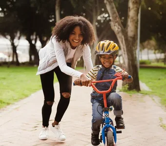 Ein Kind versucht, Fahrrad zu fahren und bekommt Hilfestellung von der Mutter