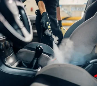 Ein Mann reinigt das Polster des Beifahrersitzes in einem Auto mit einem Dampfreiniger
