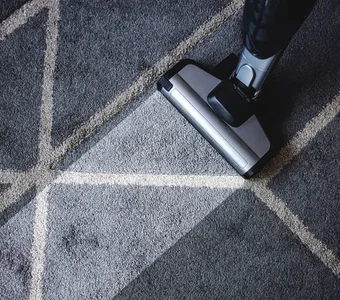 Nahaufnahme eines Dampfsaugers mit dem ein stark verschmutzter, grauer Teppich gereinigt wird