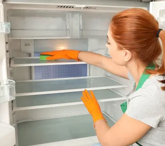 Frau reinigt mit einem Schwamm den Innenraum des leeren Kühlschranks