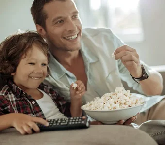 Vater und Sohn essen Popcorn, gucken Fernseher und haben Spaß.