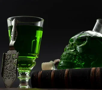 Glas mit Absinth neben einer mit Absinth gefüllten Flasche in der Form eines Totenkopfes