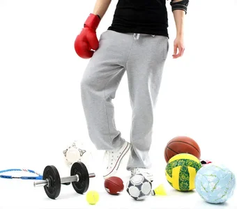 Mann in Trainingskleidung ist von unterschiedlichen Bällen und Trainingsgeräten umgeben