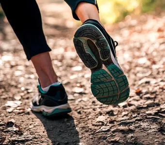 Nahaufnahme der Schuhsohle eines Laufschuhs, welche eine Läuferin auf einem Waldboden trägt