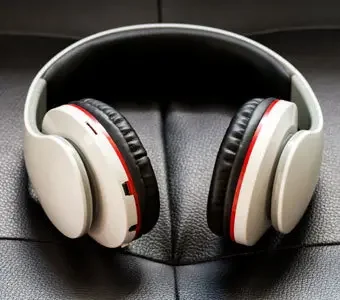 Schwarz-weiße Bluetooth-Kopfhörer liegend auf einer Fläche aus dunklem Leder