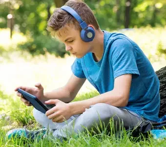 Junge mit Tablet und Funkkopfhörer sitzt auf einer Wiese