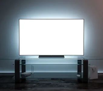 Ein Flatscreen-TV steht auf einem Glastisch in der Dunkelheit mit einem weiß leuchtenden Bildschirm