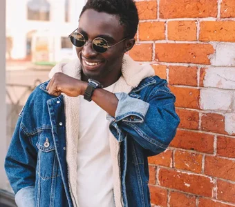 Stylischer Mann in Sonnenbrille und Jeansjacke spricht in Smartwatch am Handgelenk