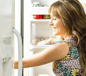 Nahaufnahme einer Frau, welche in einen geöffneten Kühlschrank greift.