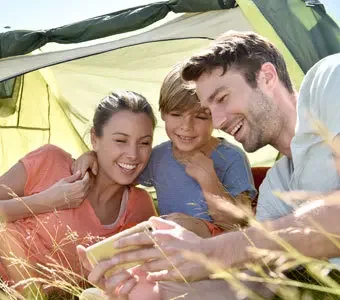 Aufnahme einer Familie, welche beim Campen auf ein Smartphone schaut.
