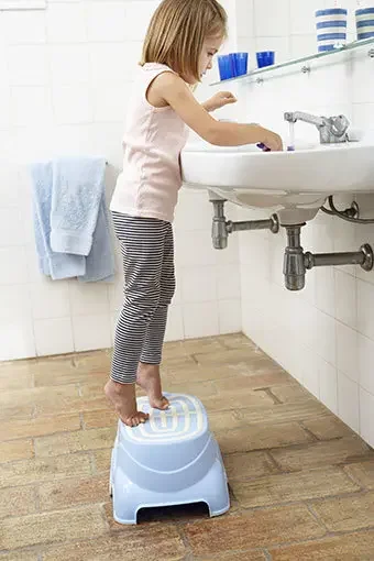 Aufnahme eines Kindes vor einem Waschbecken auf einem Badhocker.