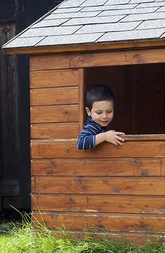 Kleiner Junge spielt in einem braunen Holzhaus.
