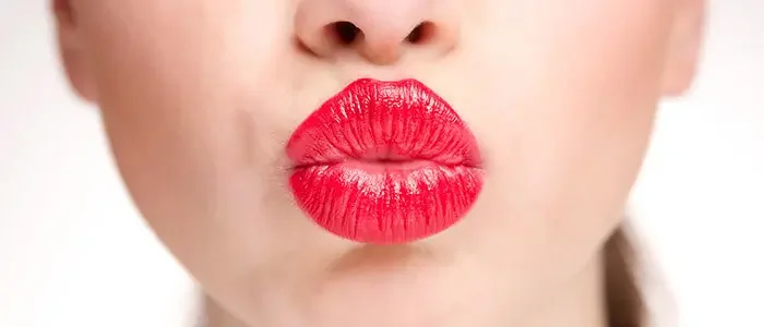 Nahaufnahme roter Lippen, welche zu einem Kussmund geformt sind.