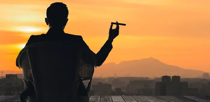 Aufnahme eines Mannes, welcher im Sonnenuntergang mit einer Zigarre sitzt.