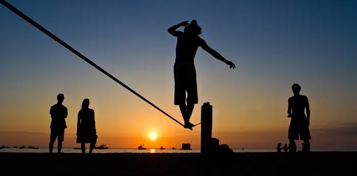 Aufnahme einer Gruppe Leute, die im Sonnenuntergang auf einer Slackline Sport machen.