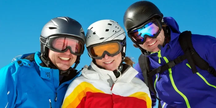Eine Frau und zwei Männer tragen bunte Skibekleidung sowie schützende Skihelme