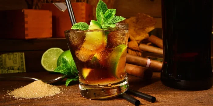 Ein Longdrink mit Rum, Cola und Limetten steht auf einem Holztisch