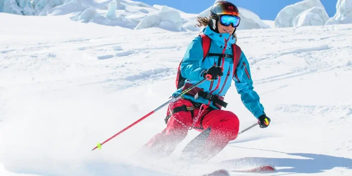 Frau mit hellblauer Skijacke und roter Skihose fährt eine Piste hinunter