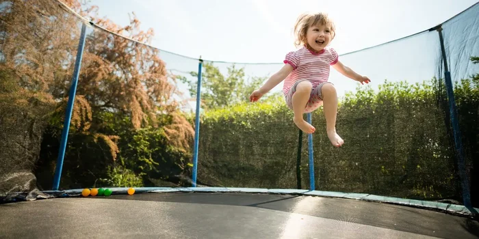 Ein Kleinkind springt im Garten auf einem großen Trampolin mit einer Umrandung
