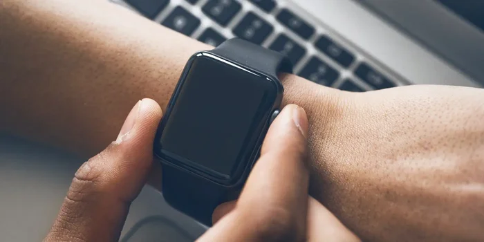 Smartwatch am Handgelenk wird von einer Person bedient und im Hintergrund ist eine Tastur zu sehen
